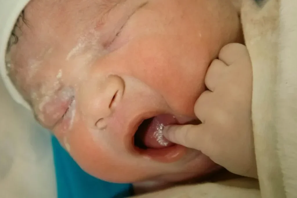 A newborn baby has a finger in its mouth.